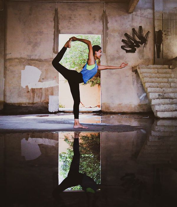 Woman holding a serene yoga pose in a dark room with cyan light accents.